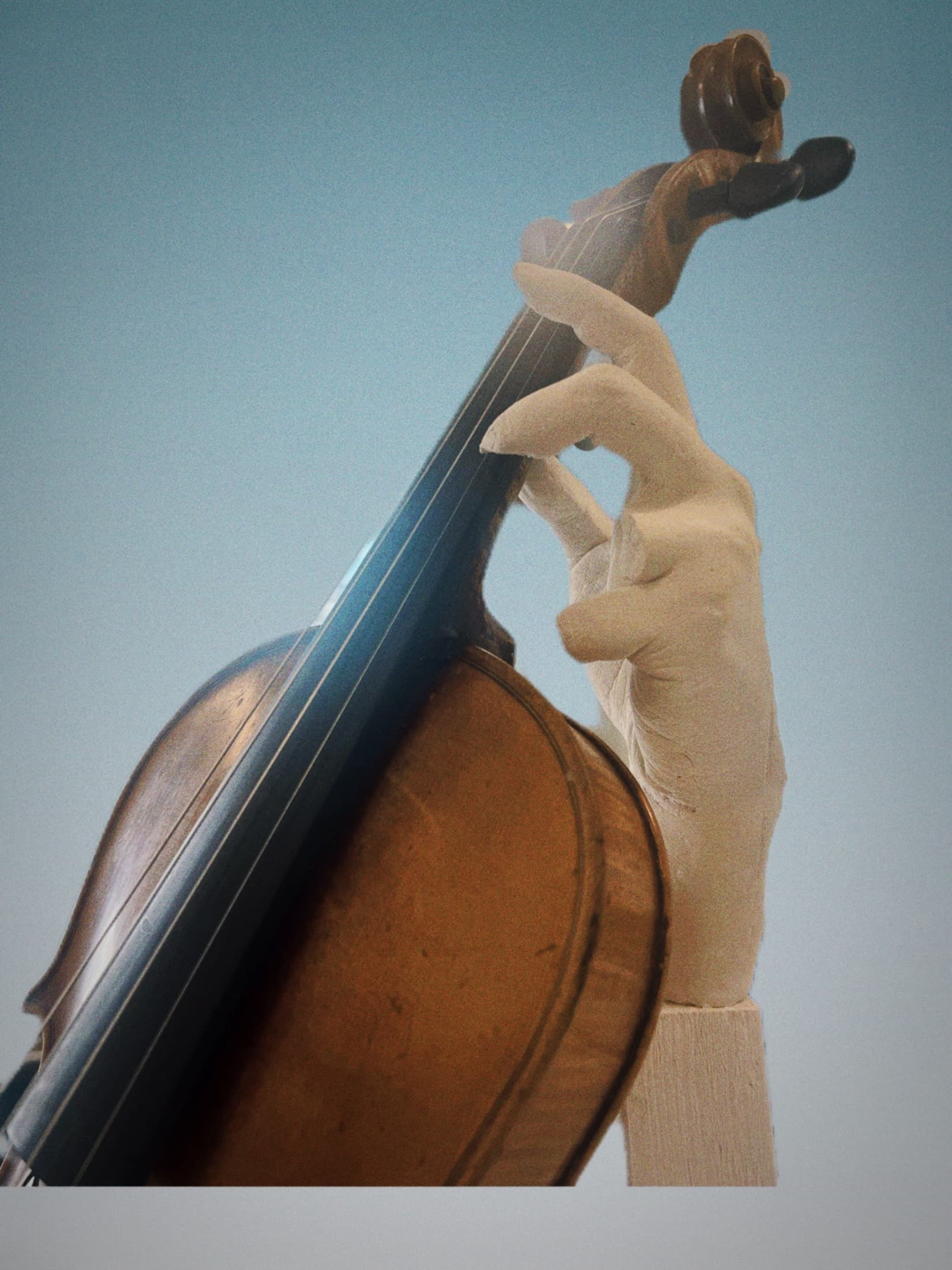 A pale sculptural hand holds the neck of a warm brown violin, posed against a muted blue background.