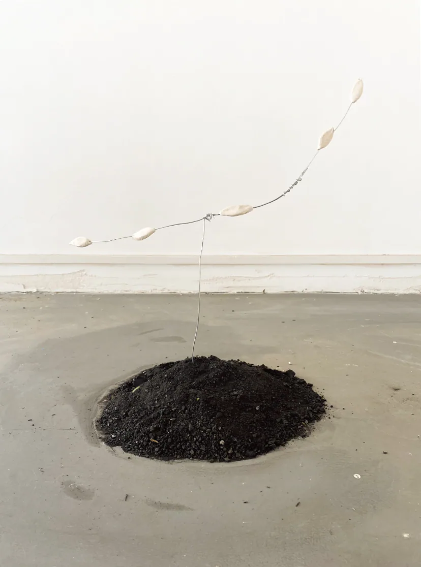 EN: Installation with a mound of coal and wire-suspended clay leaves, symbolizing falling leaves as both death and the first step toward renewal through geological time.