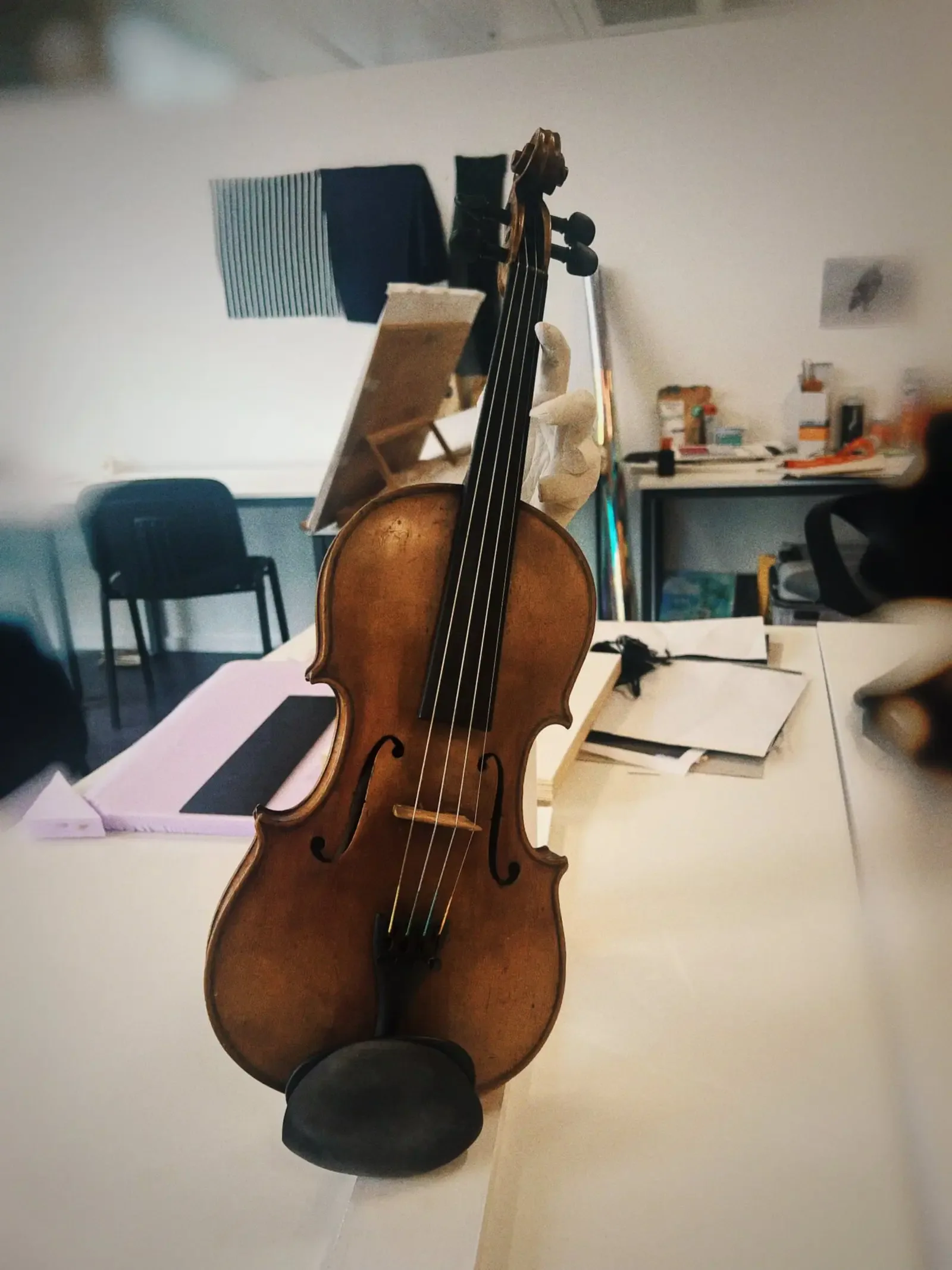 The violin and sculptural hand displayed upright on a working studio table.
