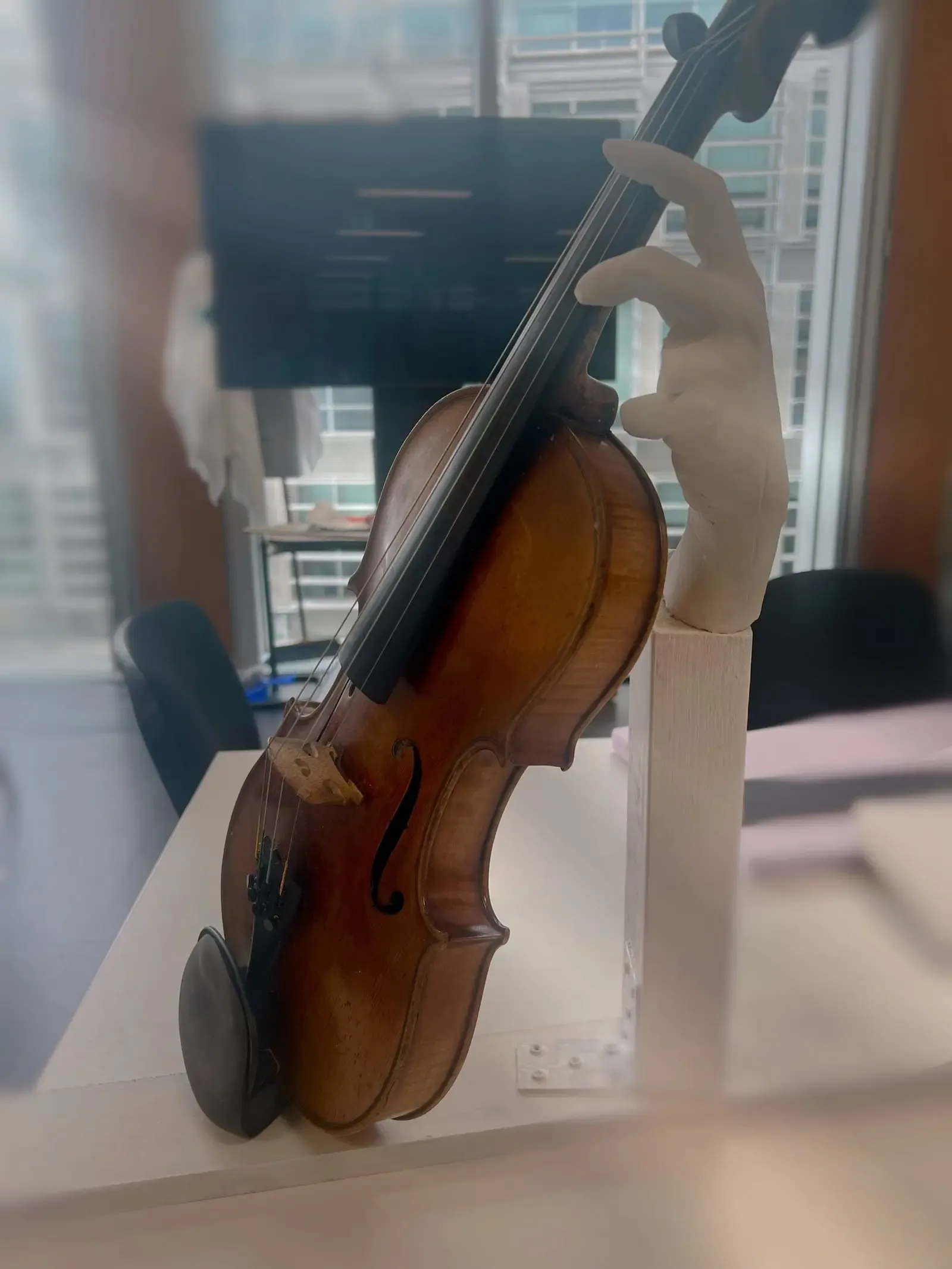 Installation view of the violin held by a sculptural hand beside a studio window.